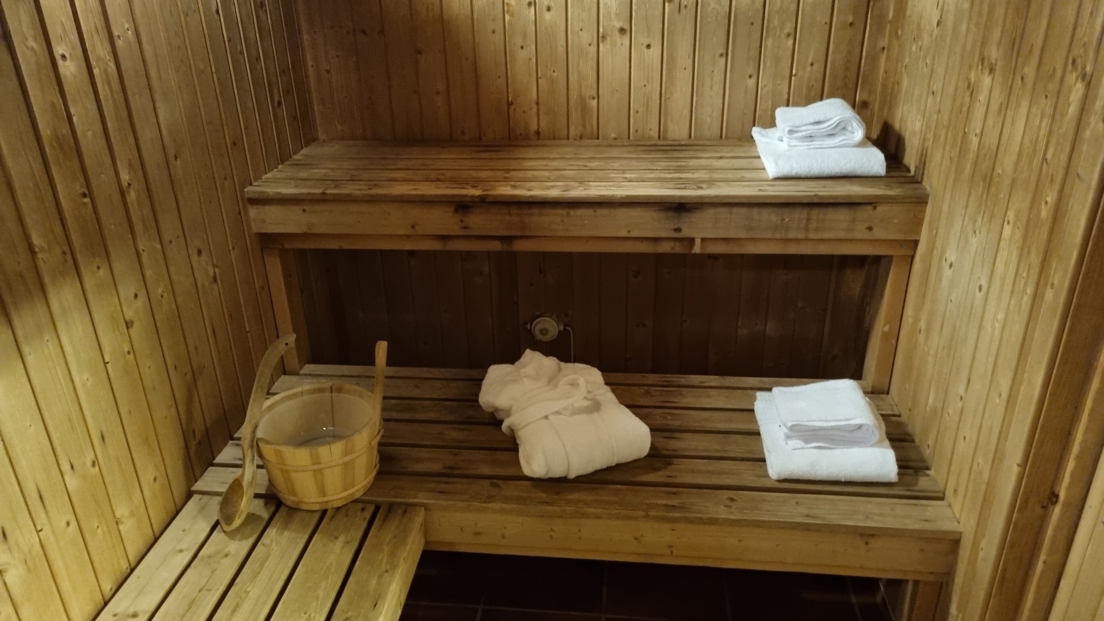 A wooden sauna with benches, a wooden bucket, and towels.
