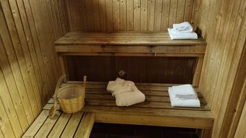 A wooden sauna with benches, a wooden bucket, and towels.