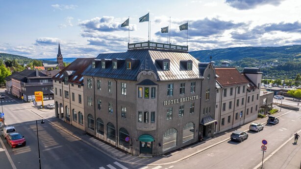 A historic building with a prominent tower, a sign reading "HOTEL BREISSEIS," and a view of the surrounding town and hills. - Hotel Breiseth (Lillehammer)