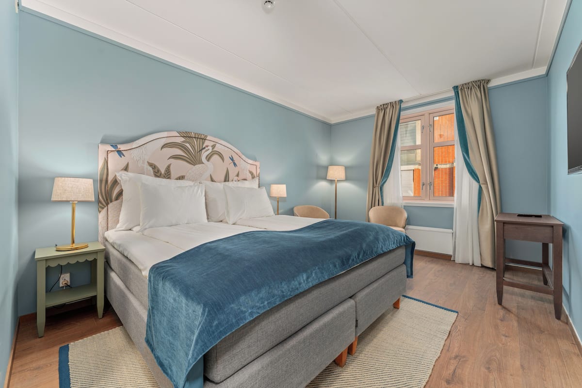 A bedroom with a bed, bedside lamps, a window with curtains, and a small table.
