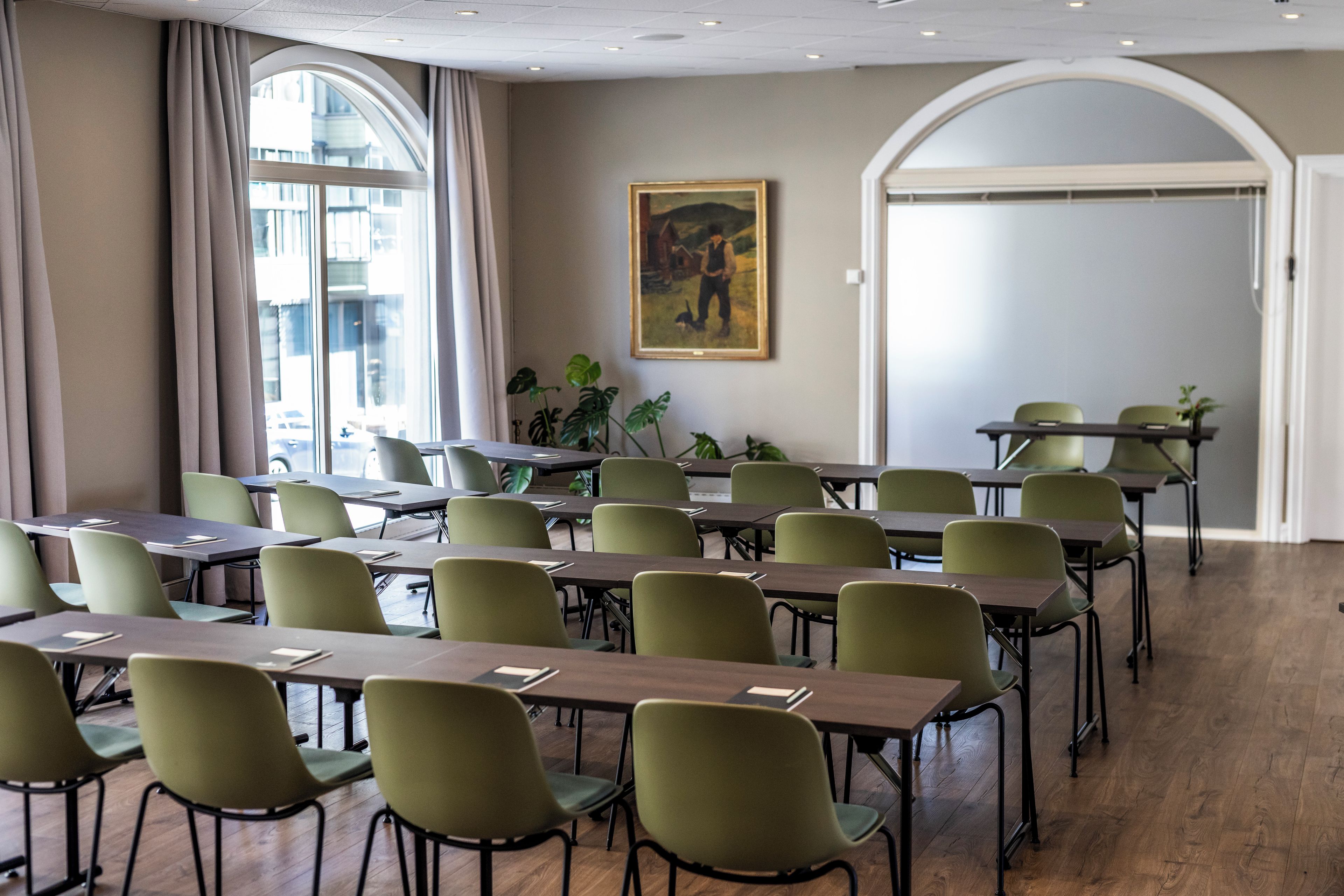 Une salle de conférence équipée de tables et de chaises, de grandes fenêtres et ornée d’un tableau au mur.