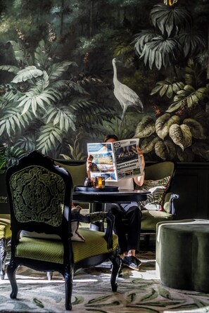 Una persona leyendo un periódico en una habitación con un gran mural de un bosque y un ave.