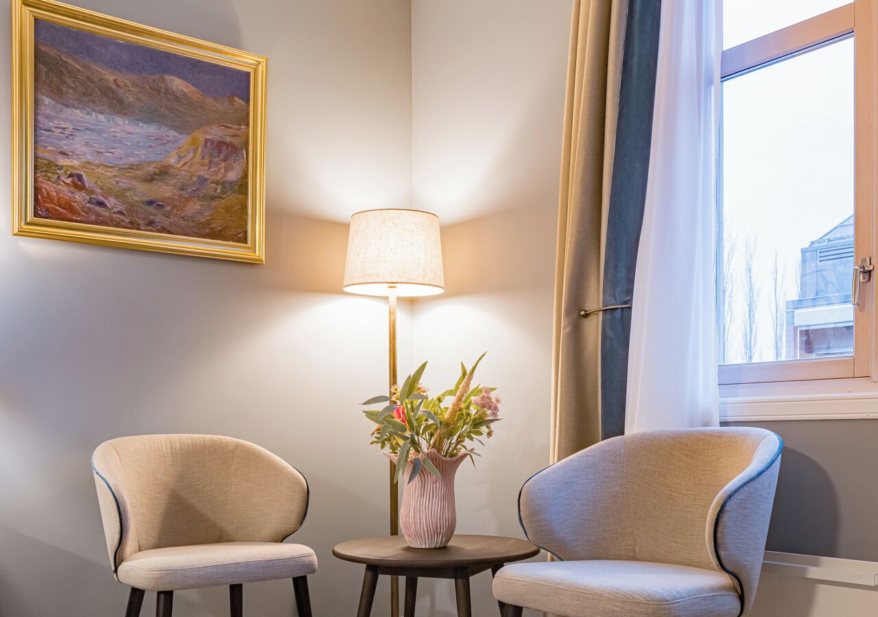 A room with two chairs, a lamp, a vase with flowers, and a painting on the wall.