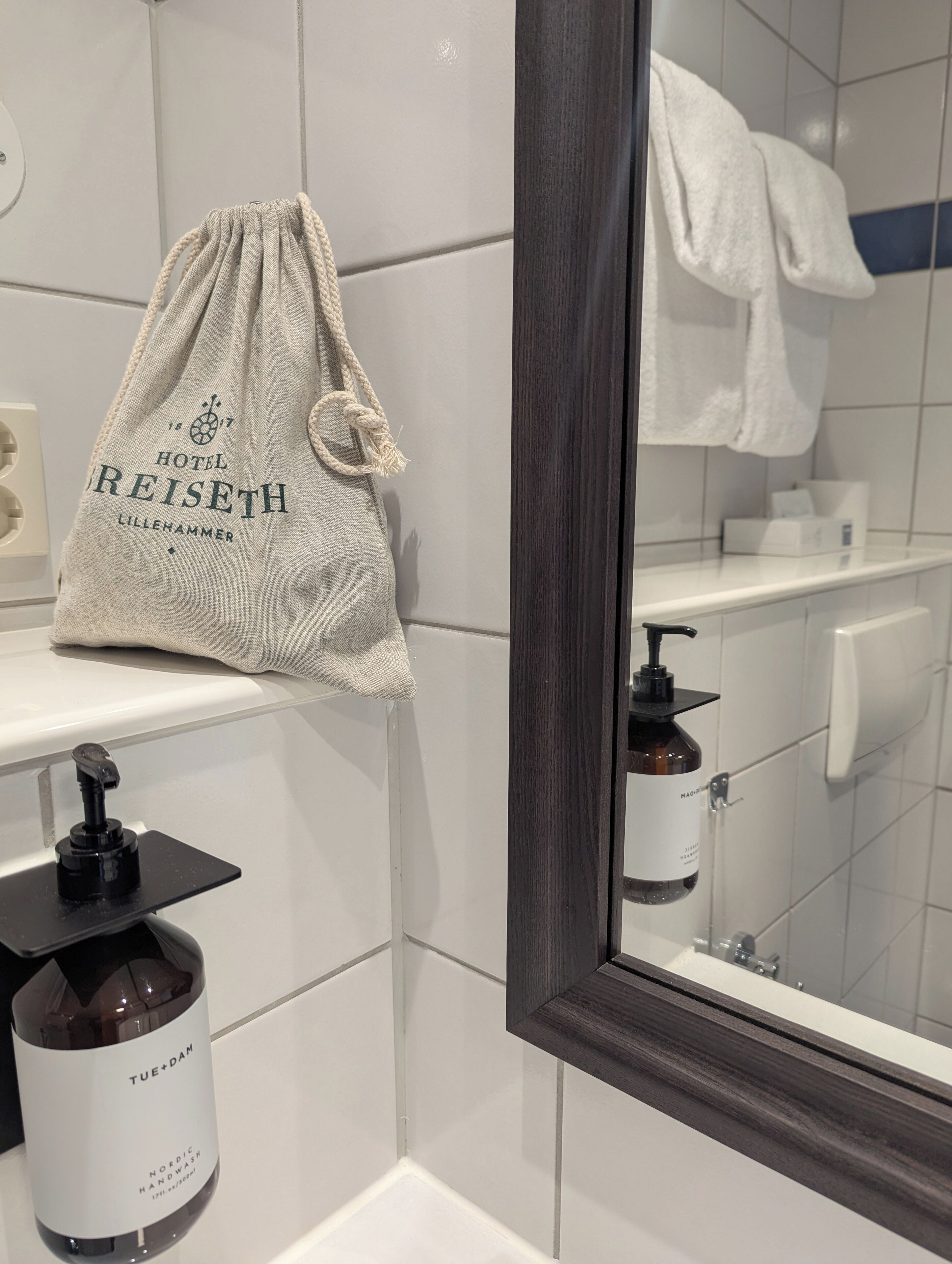 A bathroom with a white sink, a mirror, a towel hanging on the wall, and a bottle of hand soap.