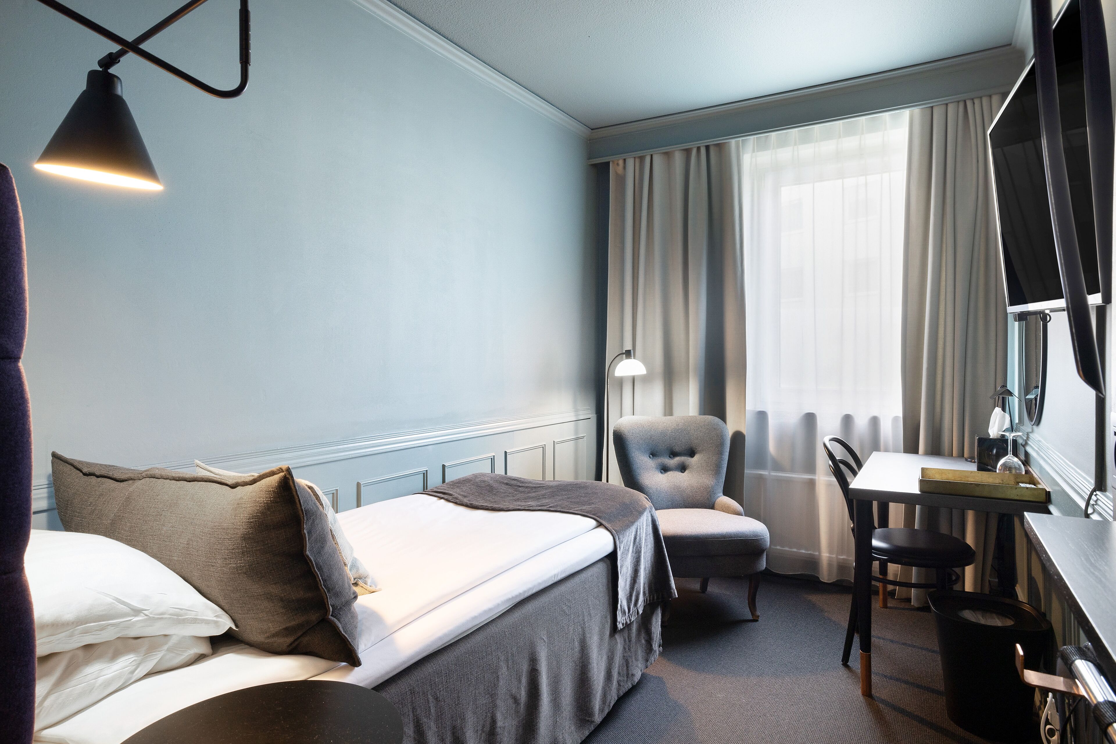 Habitación de hotel con cama, escritorio, silla y ventana con cortinas.