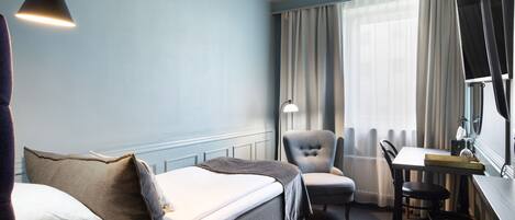 Habitación de hotel con cama, escritorio, silla y ventana con cortinas.