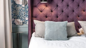 Quarto com cabeceira estofada, mesa de cabeceira com abajur e papel de parede floral.