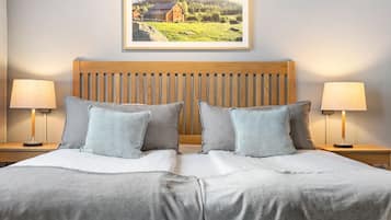 A neatly made bed with a wooden headboard, two bedside lamps, and a framed landscape picture on the wall.