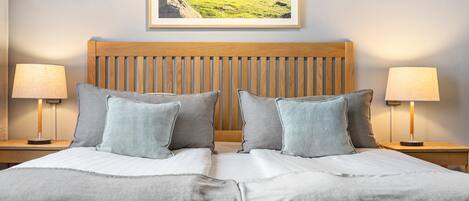 A neatly made bed with a wooden headboard, two bedside lamps, and a framed landscape picture on the wall.