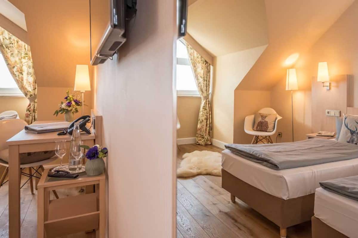 Een hotelkamer met twee bedden, een bureau met telefoon, een stoel en een wandlamp.