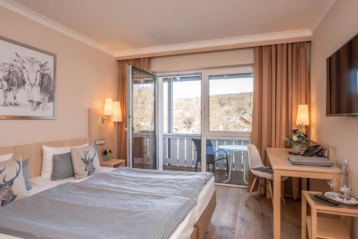 Een hotelkamer met een groot bed, een bureau met stoel, een balkon met tafel en stoelen, en een televisie aan de muur.