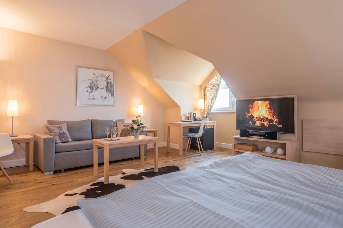 Een moderne hotelkamer met een loft-plafond, een gezellige zithoek, een flatscreen-televisie, een bureau met stoel, en een groot bed met een koeienhuidtapijt.
