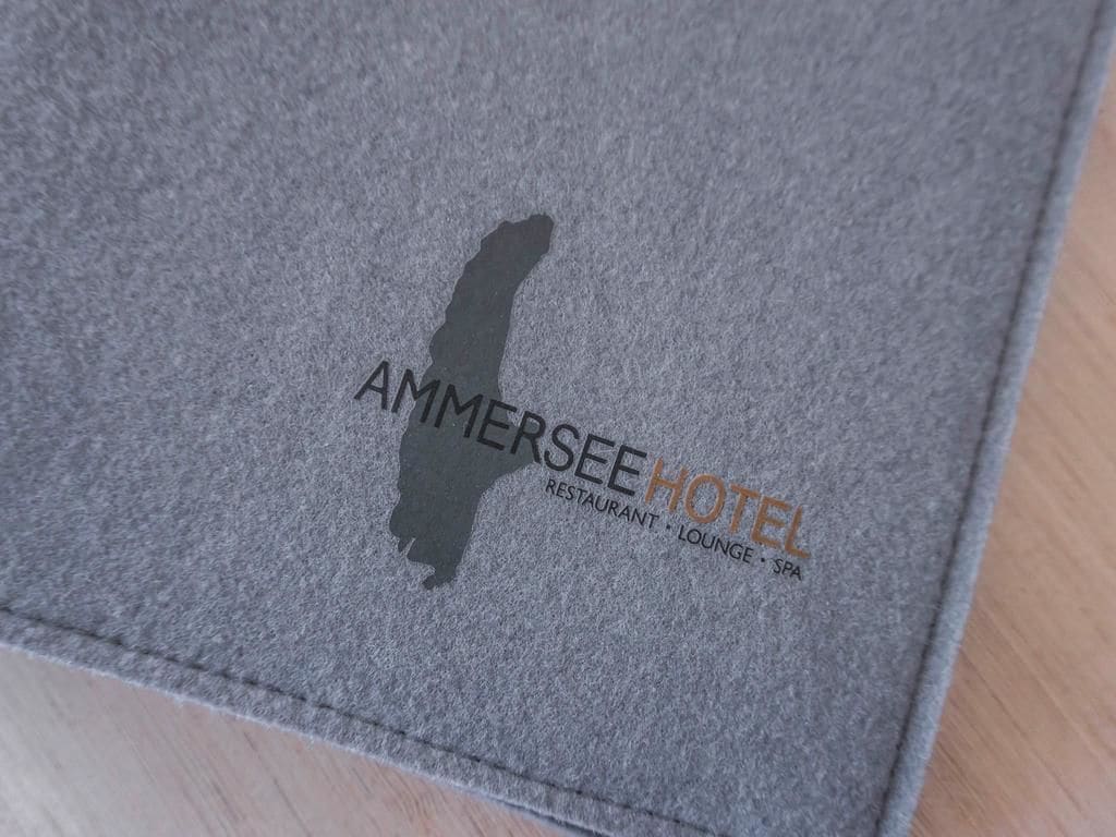 Een grijze brochure met de tekst 'AMMERSEE HOTEL RESTAURANT, LOUNGE, SPA' en een berg in silhouet.
