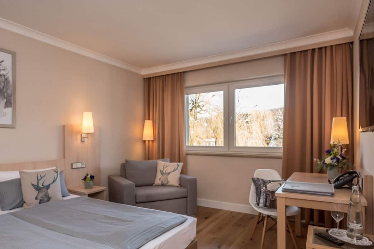 Een hotelkamer met een bed, een bureau, een stoel, een lamp en een raam met gordijnen.