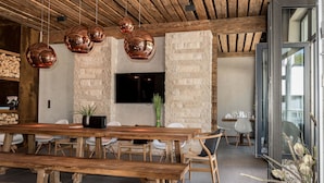 Un comedor moderno con una gran mesa de madera, varias sillas y lámparas colgantes de cobre.