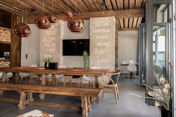 A modern dining area with a large wooden table, multiple chairs, and copper pendant lights.