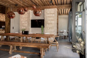 Uma sala de jantar moderna com uma grande mesa de madeira, várias cadeiras e luminárias pendentes de cobre.