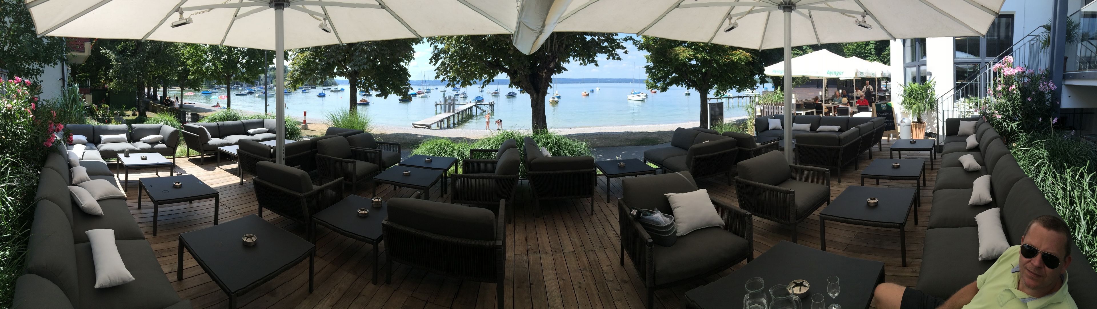 Uma área de estar externa com mesas e cadeiras, com vista para um corpo de água e barcos.