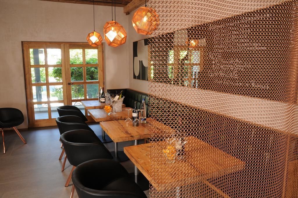 Un restaurante con mesas de madera y sillas negras, un amplio ventanal con vistas, y lámparas colgantes naranjas.