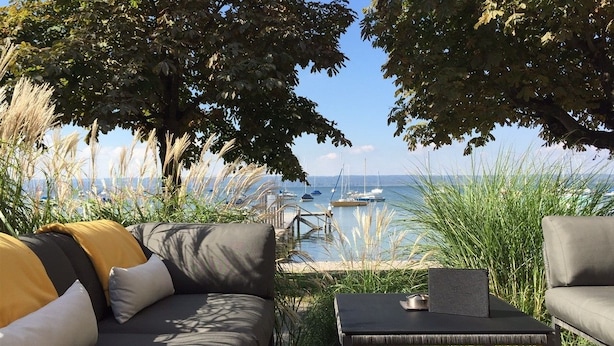 Un área de estar al aire libre con un sofá y una mesa, con vista a un puerto deportivo y barcos.