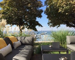 Área externa com sofás e uma mesa, com vista para uma marina e barcos.