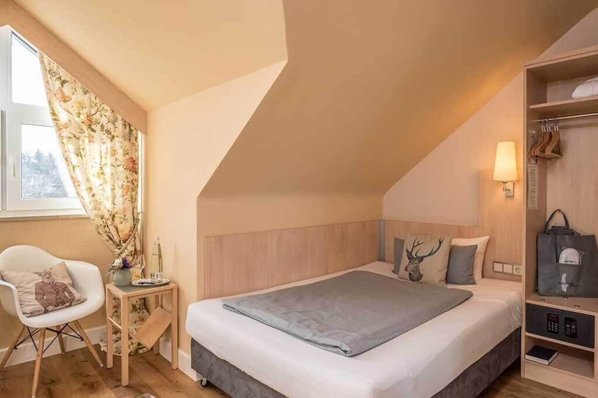 Een slaapkamer met een bed, een stoel, een nachtkastje, een lamp, een kledingkast en een raam met gordijnen.