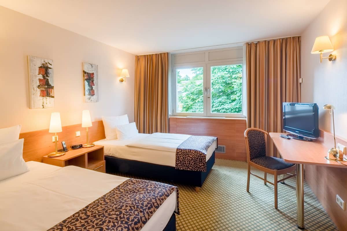 A hotel room with two beds, a desk with a television, and a window with curtains.