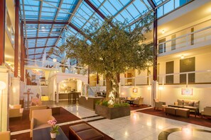 A spacious hotel lobby with a large tree, seating areas, and a glass ceiling. - Best Western Plus Hotel Fellbach-Stuttgart (Fellbach)
