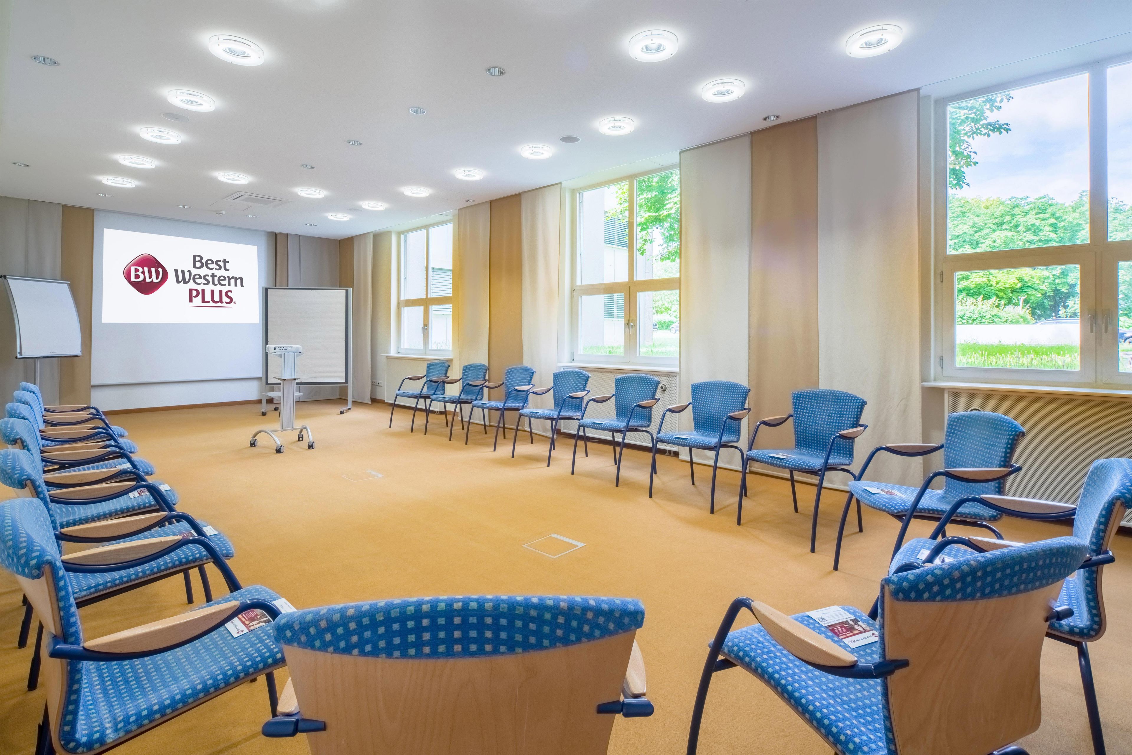 A conference room with a projector screen displaying 'BW Western PLUS' logo, multiple rows of blue chairs, and large windows with natural light.