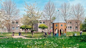 Un parc avec un kiosque, une aire de jeux et, au fond, un bâtiment doté de nombreuses fenêtres.