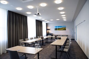 Un salón de conferencias con una larga mesa, sillas, un proyector y un cuadro en la pared.