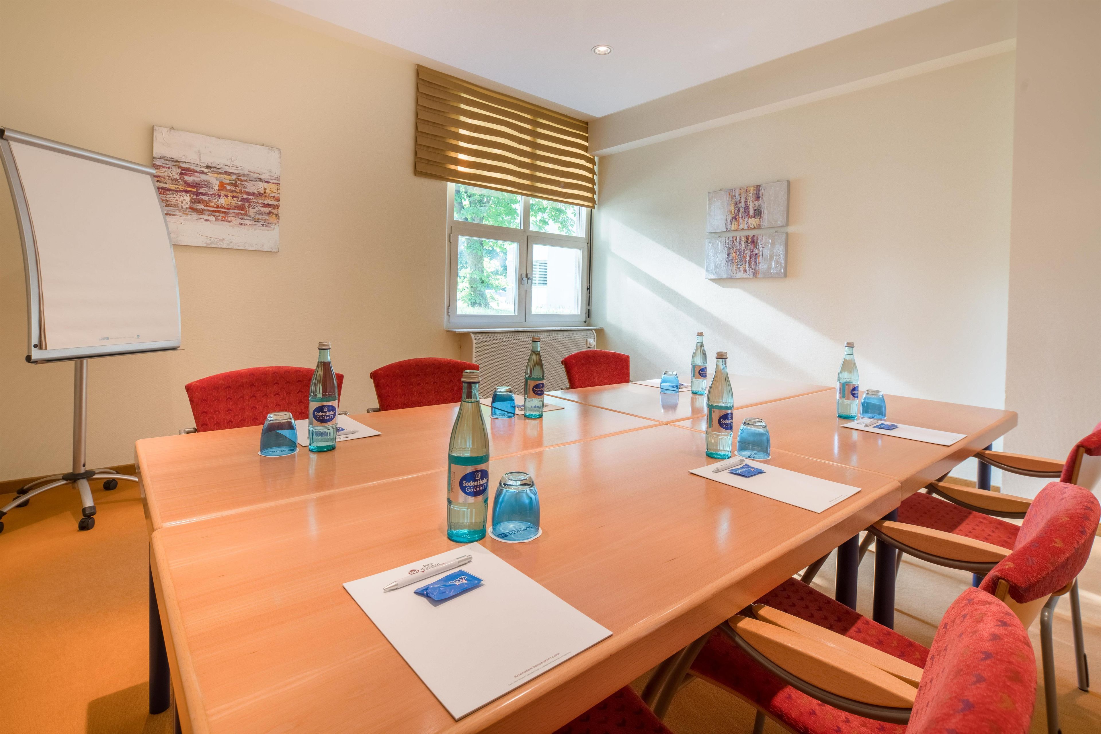 A conference room with a long table, red chairs, and water bottles.