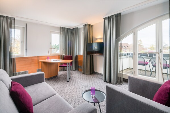 A hotel room with a sofa, a small table, a TV, and a balcony with chairs. - Best Western Plus Hotel Fellbach-Stuttgart (Fellbach)