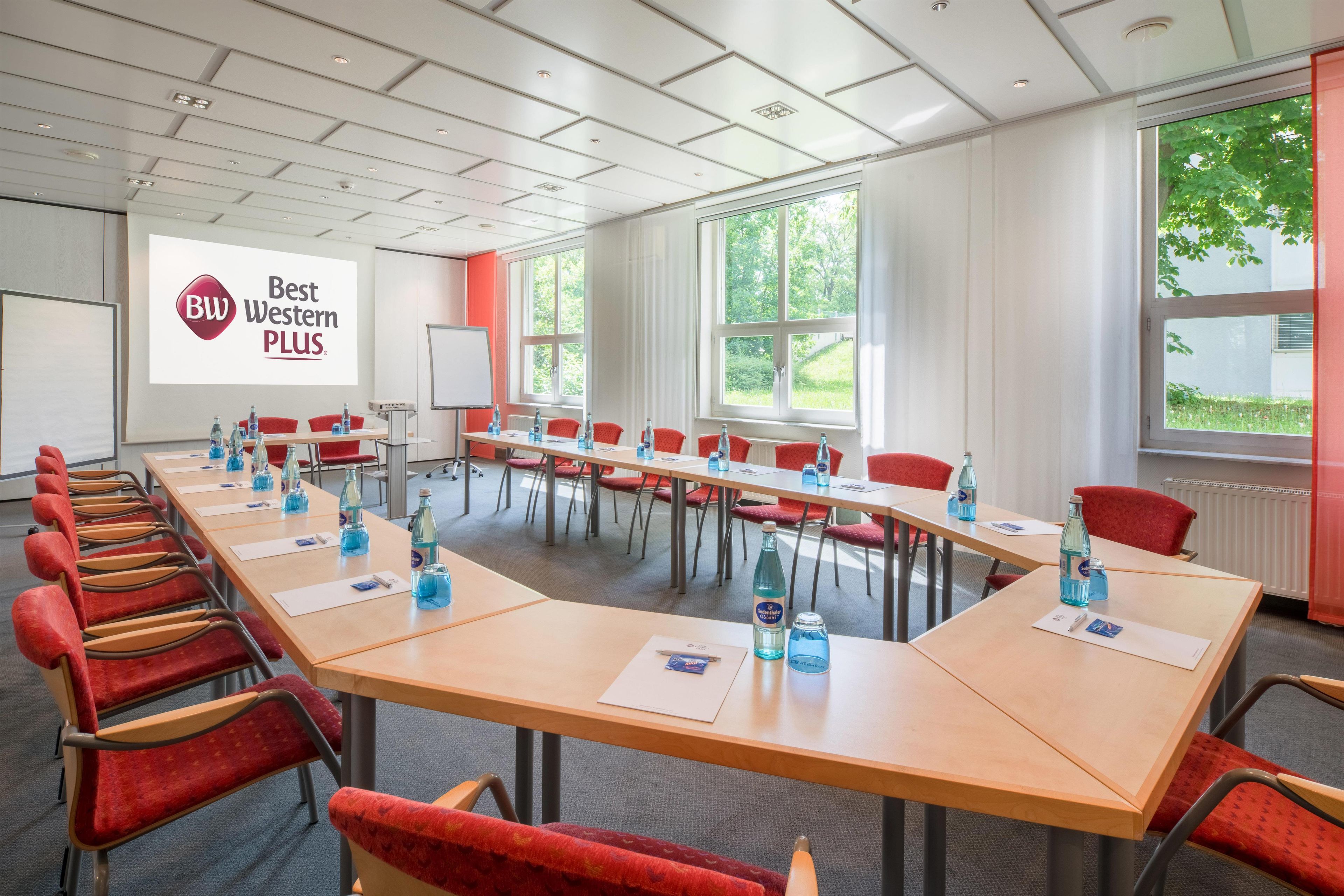 A conference room with a long table, red chairs, and a projector screen displaying 'Best Western PLUS'.