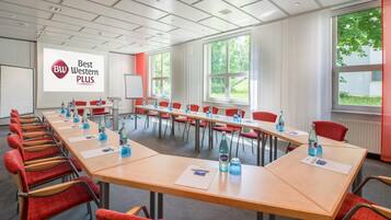 A conference room with a long table, red chairs, and a projector screen displaying 'Best Western PLUS'.