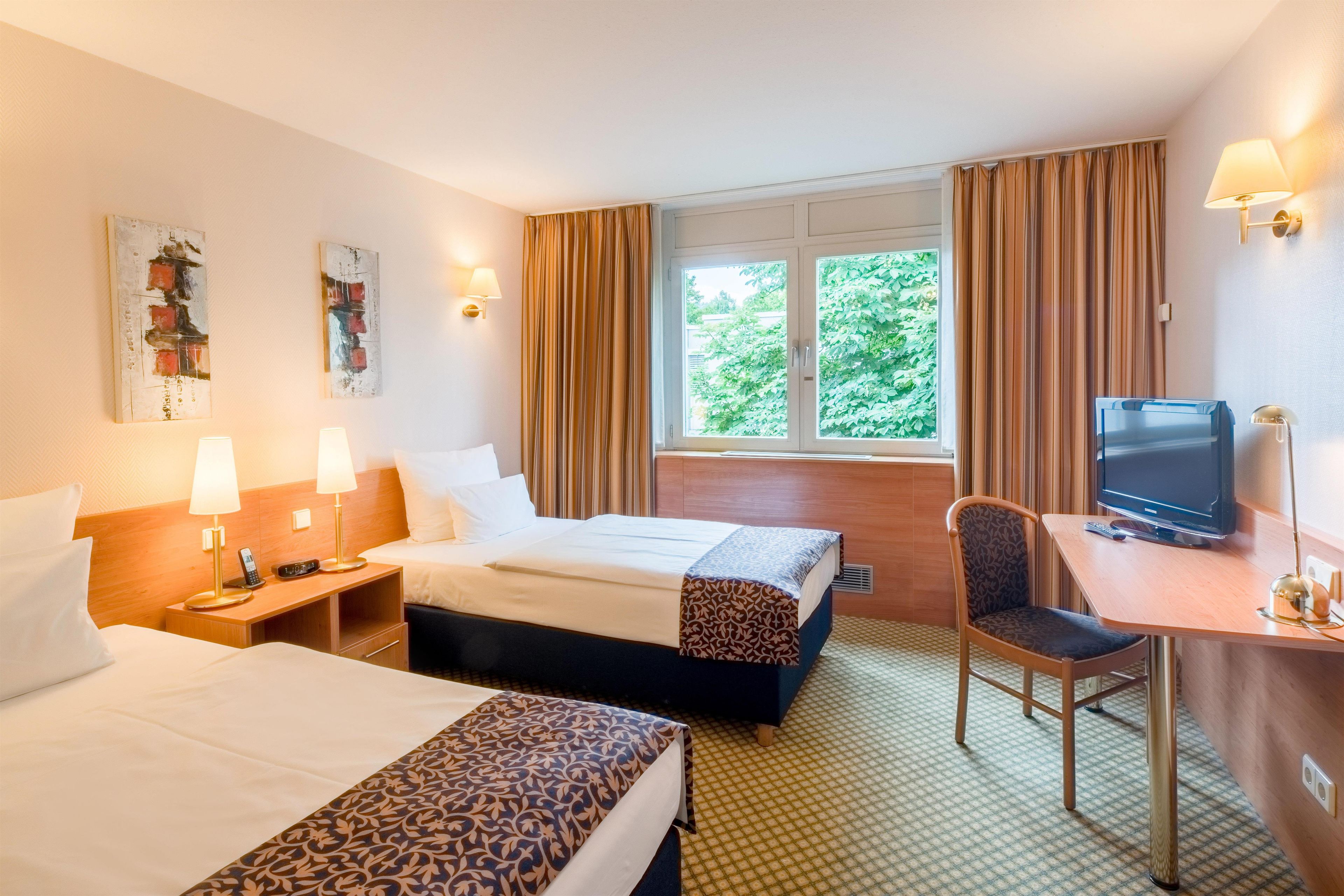 A hotel room with two beds, a desk with a television, a chair, and a window with curtains.
