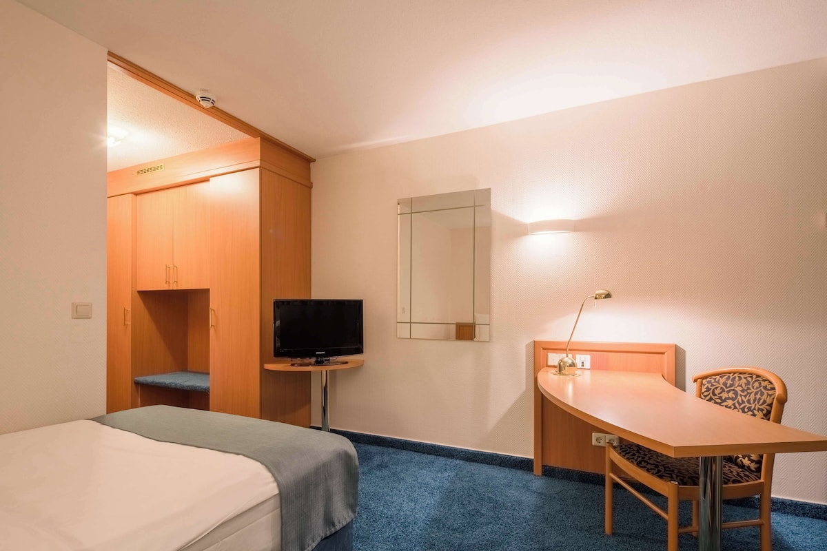 A hotel room with a bed, a desk with a chair, a television, and a wardrobe.