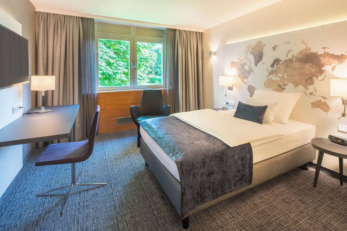 A hotel room with a bed, desk, chair, and a world map on the wall.