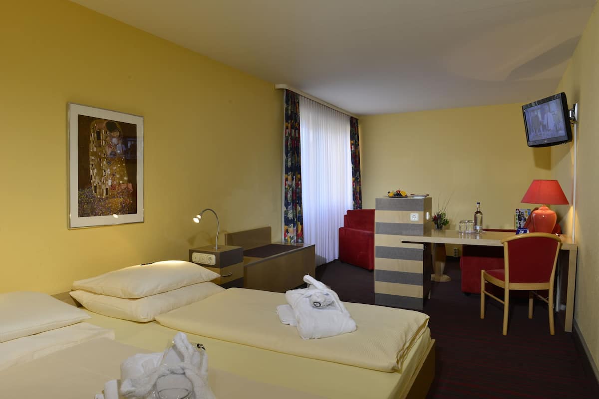 A hotel room with two beds, a desk, a chair, a TV, and a painting on the wall.