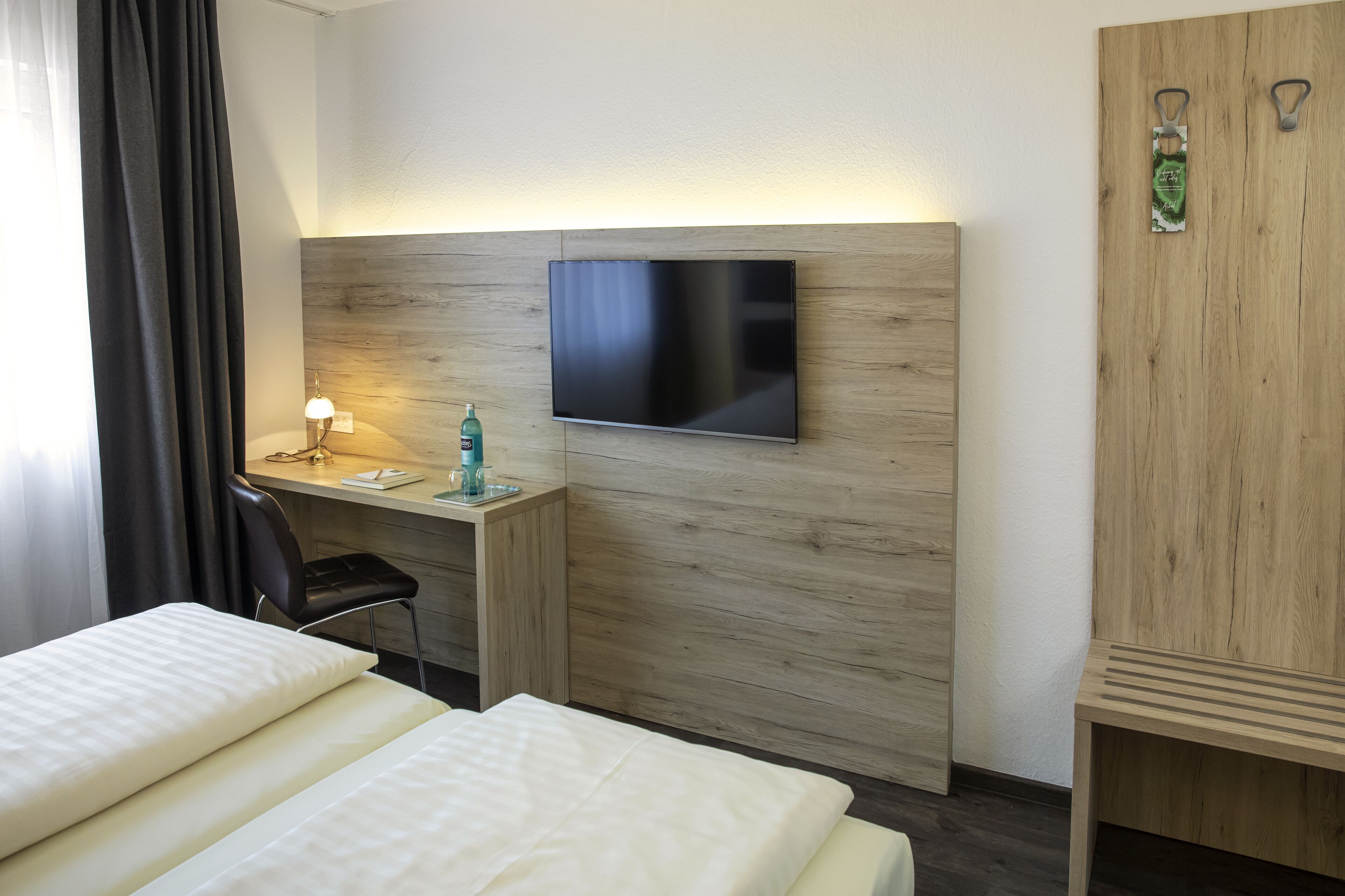 Habitación de hotel con cama, escritorio con silla, televisor montado en una pared de madera y armario.