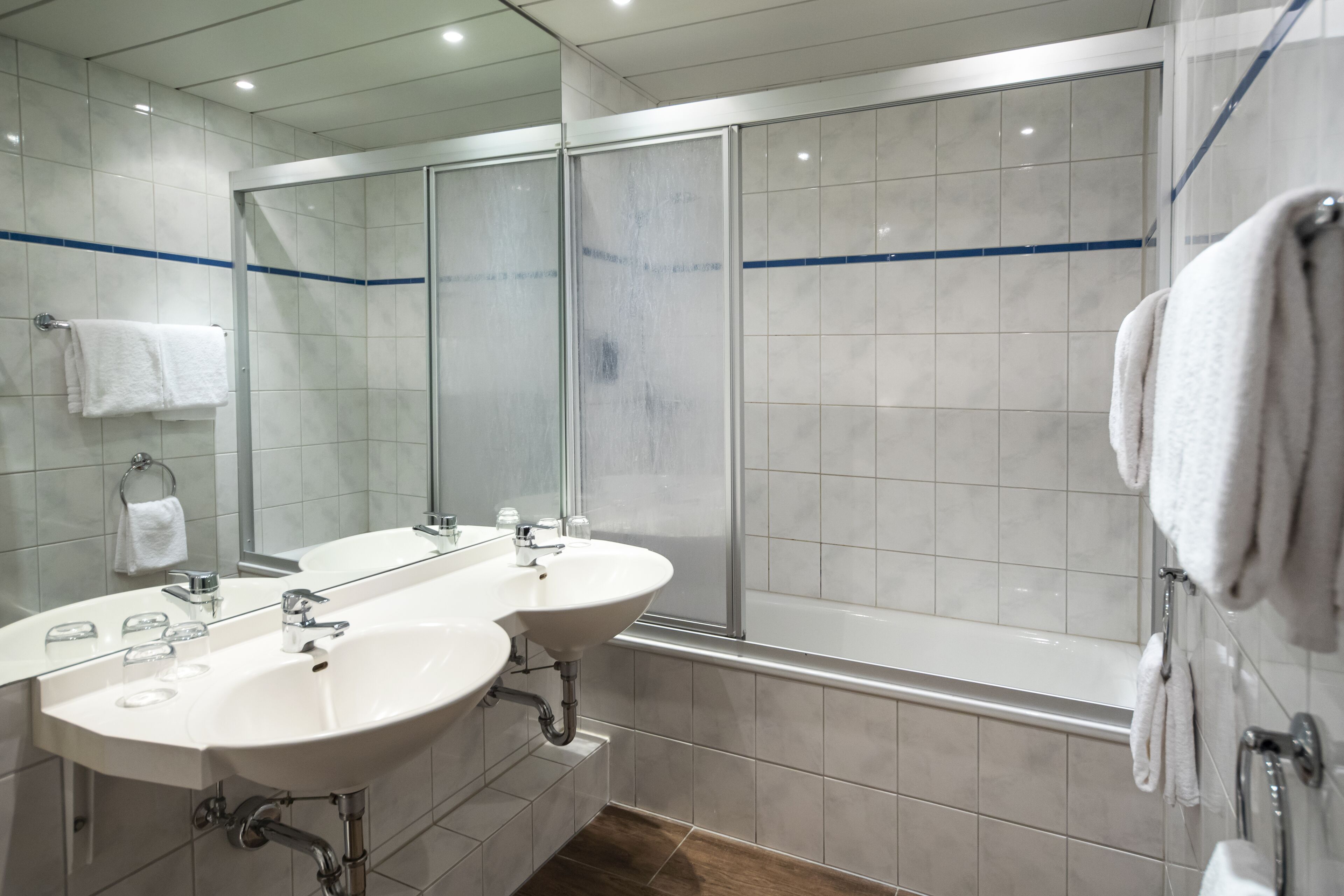 Un baño moderno con dos lavamanos, un espejo grande y una ducha con cerramiento de vidrio.