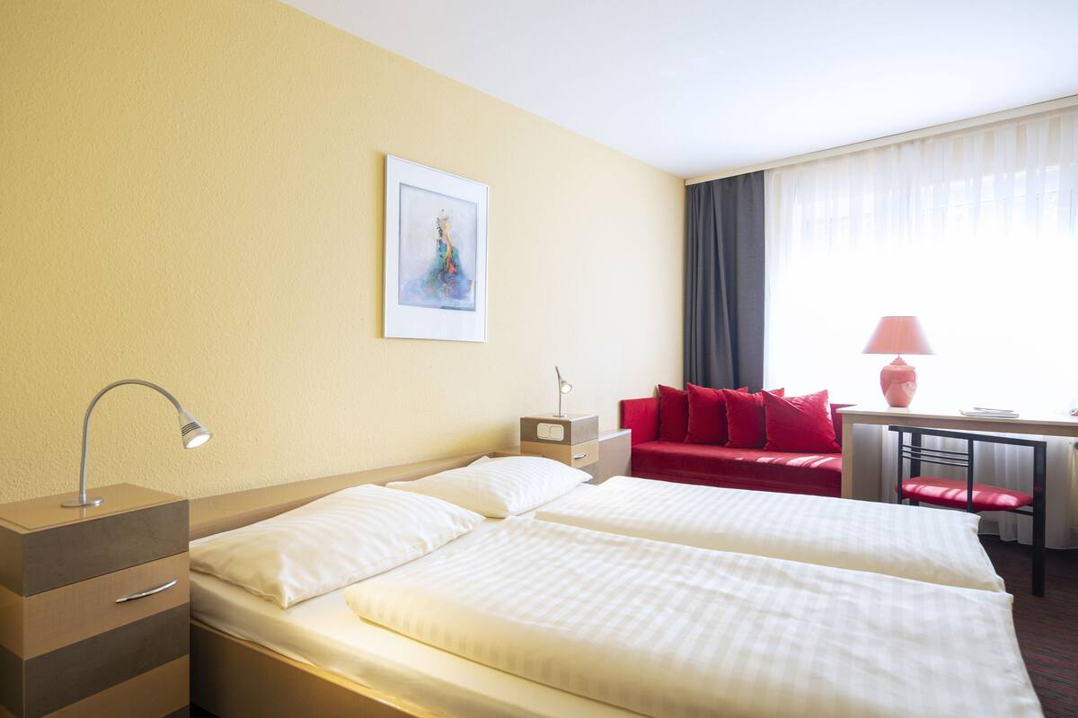 A hotel room with two beds, a desk, a chair, a lamp, a nightstand, and a painting on the wall.