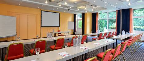 A conference room with long tables, red chairs, and a projector screen.