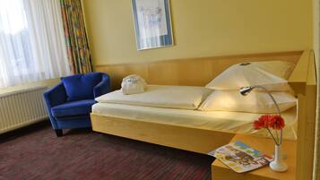 A hotel room with a single bed, a blue armchair, a radiator, a window with curtains, and a framed picture on the wall.