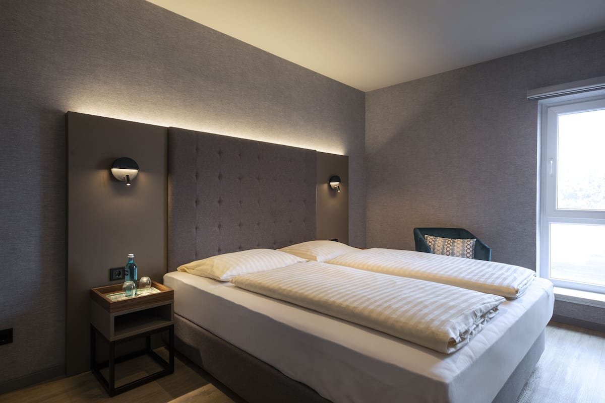 A modern hotel room with a large bed, two bedside tables, and a window providing natural light.