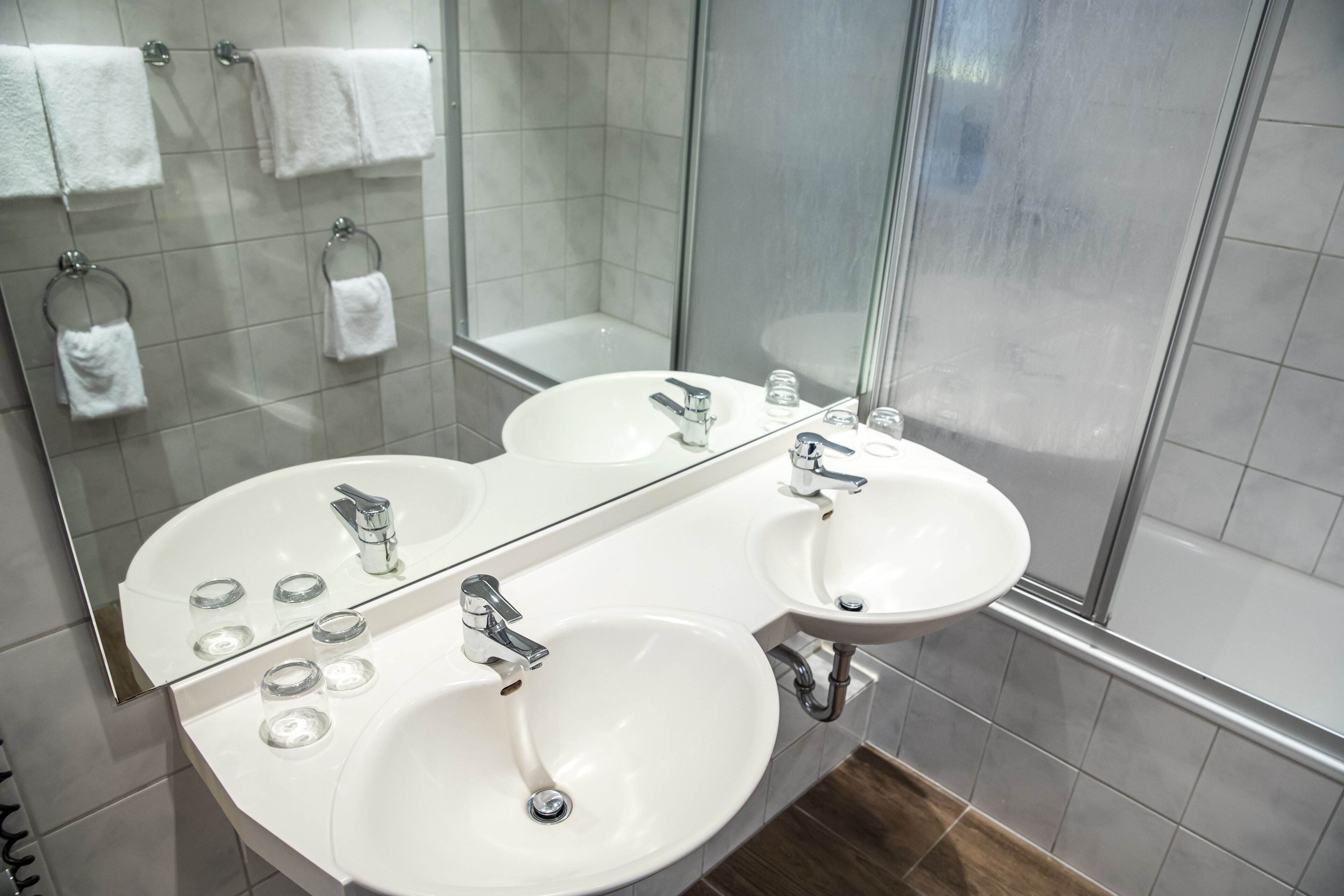 A modern bathroom with two sinks, a glass shower enclosure, and a large mirror.