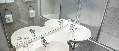 A modern bathroom with two sinks, a glass shower enclosure, and a large mirror.