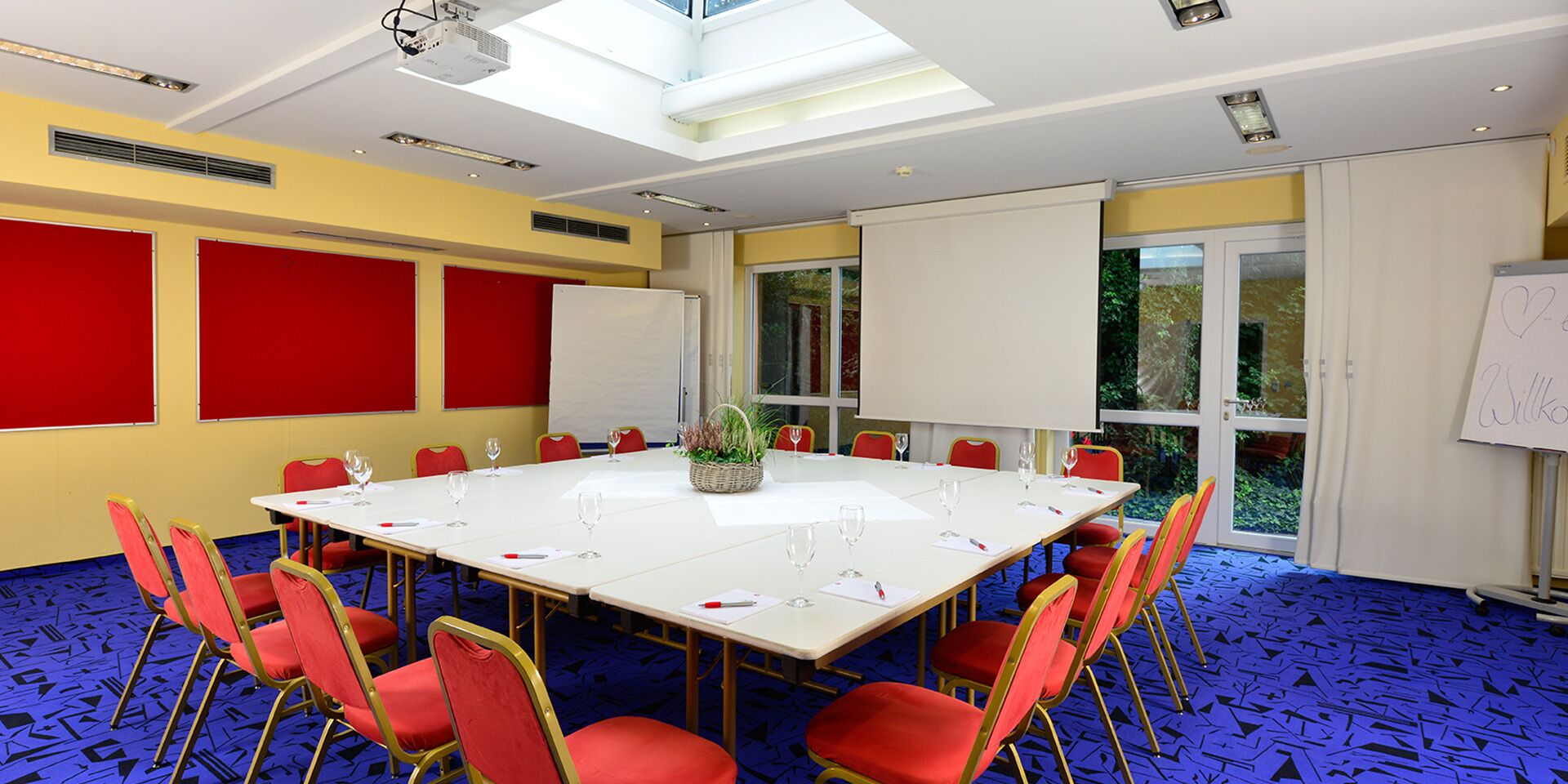 A conference room with a large table, red chairs, a whiteboard, and a projector.