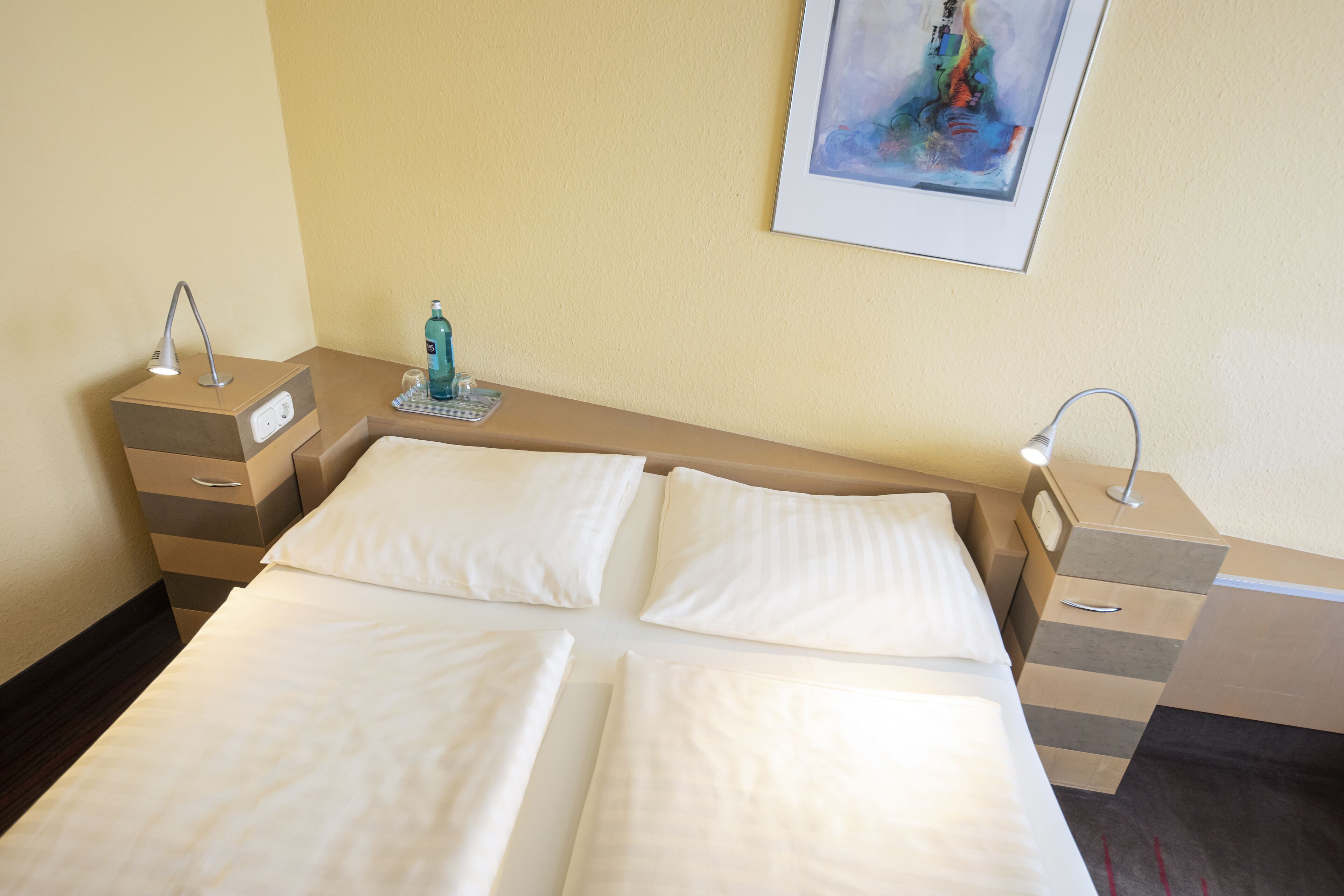 A hotel room with a bed, bedside tables, a nightstand, a clock, and a painting on the wall.