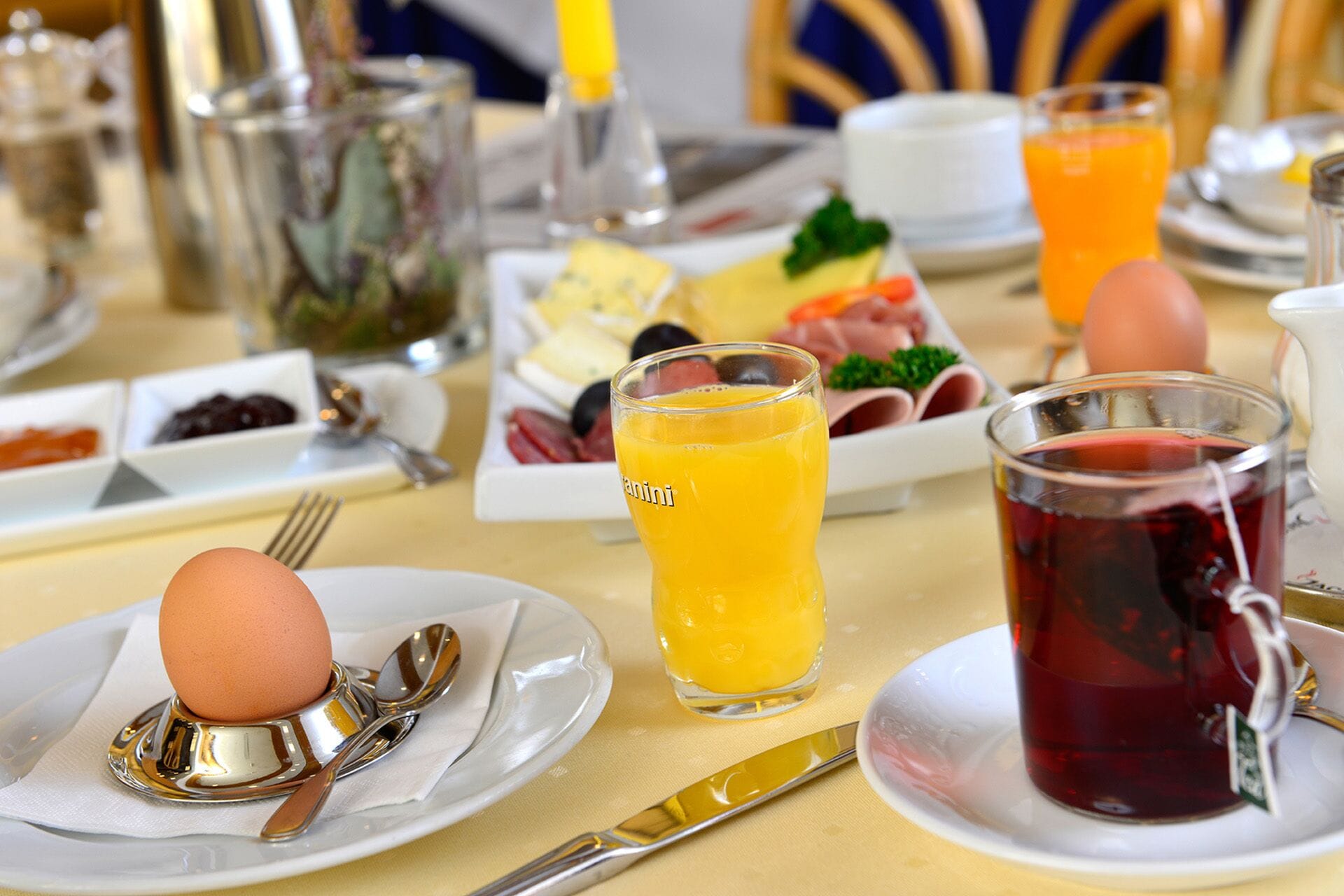 A breakfast setting with plates of eggs, toast, and fruit, along with glasses of orange juice and tea.